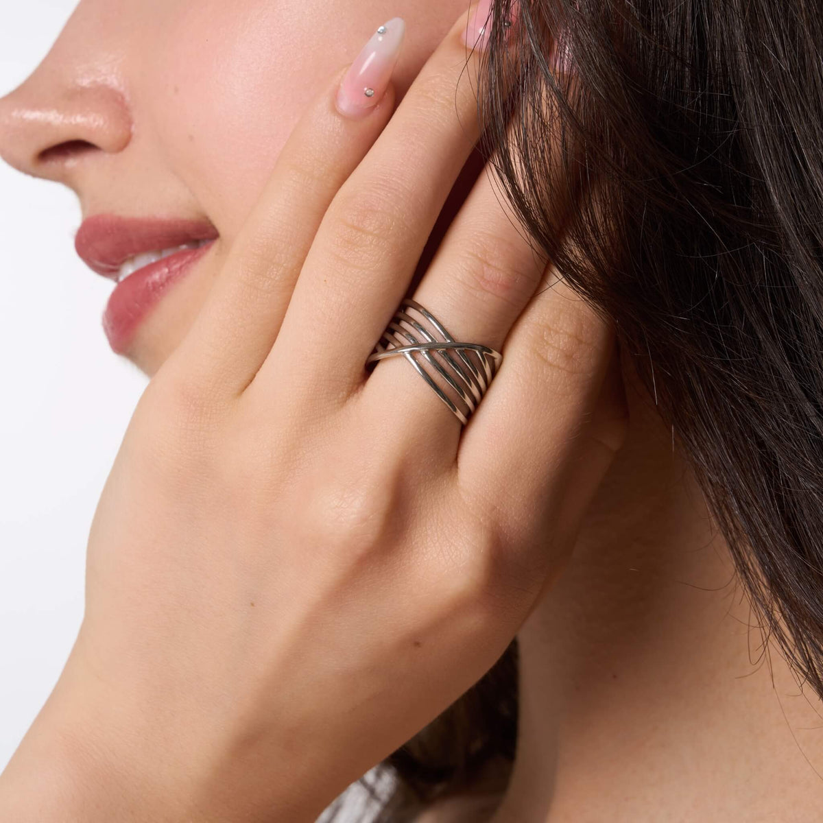 Silver chunky crossover ring worn on a hand beside the face